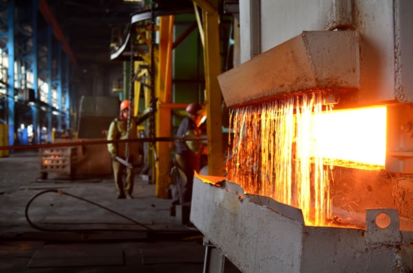 Heat treatment of metal in industrial furnace with workers overseeing.